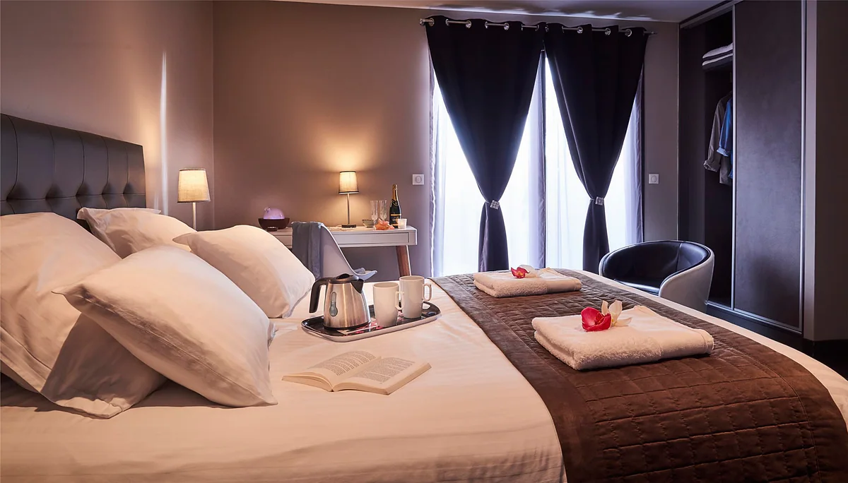 La chambre Camphre, son grand lit, les oreillers et les rideaux sombres sur la baie vitrée