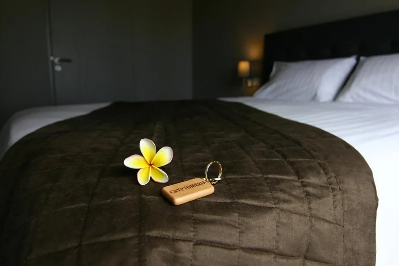 Une fleur de frangipanier et la clé posées sur le lit de la chambre Cryptoméria