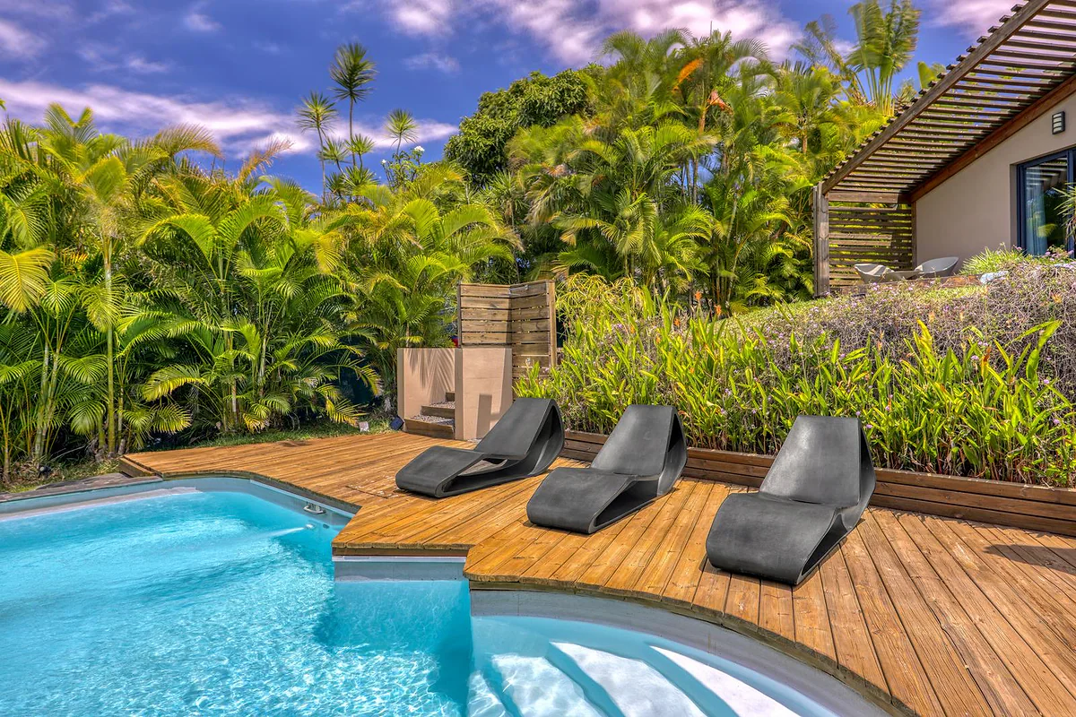 La piscine et son deck en bois, au milieu du jardin tropical