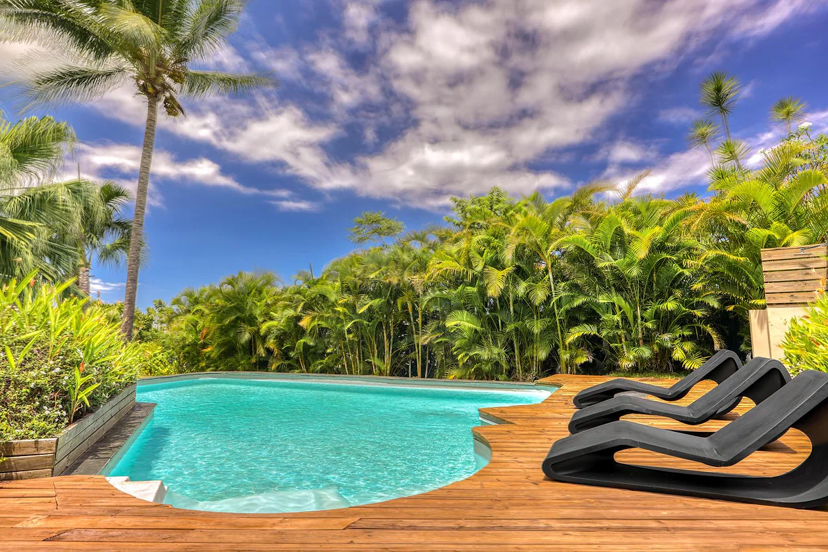 La piscine en forme libre, ses transats et le jardin sous le ciel bleu
